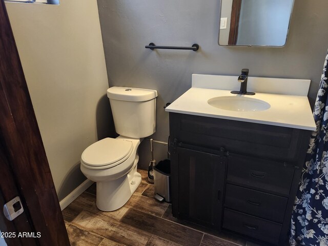 bathroom with toilet, vanity, wood finished floors, and baseboards