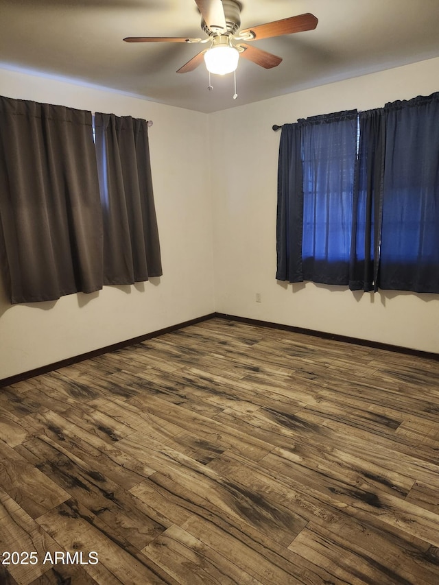 spare room featuring dark wood-style flooring, ceiling fan, and baseboards