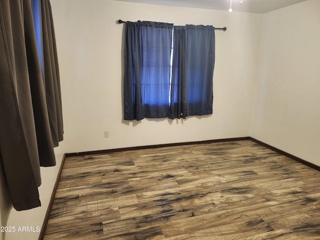 spare room with baseboards and wood finished floors