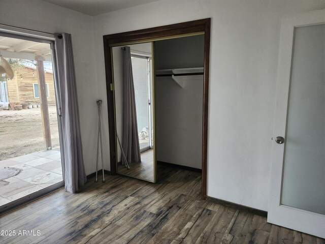 unfurnished bedroom featuring a closet, baseboards, access to outside, and wood finished floors