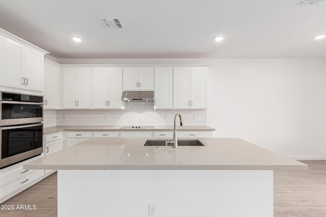 kitchen featuring white cabinetry, sink, light hardwood / wood-style flooring, an island with sink, and double oven