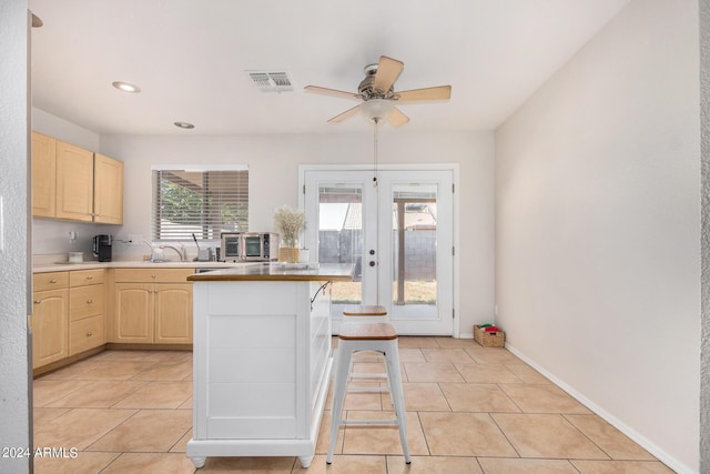 kitchen with visible vents, light brown cabinetry, a kitchen breakfast bar, french doors, and light tile patterned flooring