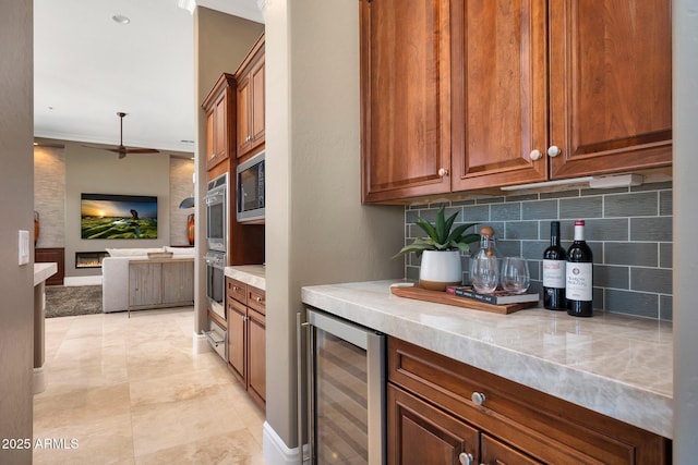 kitchen with light countertops, decorative backsplash, built in microwave, beverage cooler, and a lit fireplace