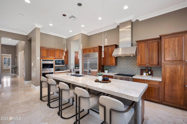 kitchen with a sink, visible vents, appliances with stainless steel finishes, wall chimney exhaust hood, and brown cabinetry