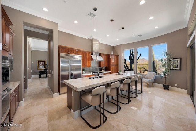 kitchen with visible vents, brown cabinetry, stainless steel appliances, wall chimney range hood, and a sink