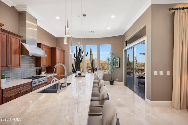 kitchen featuring brown cabinets, ornamental molding, a sink, wall chimney range hood, and light stone countertops