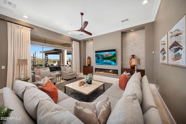 living room featuring baseboards, visible vents, ornamental molding, and a glass covered fireplace