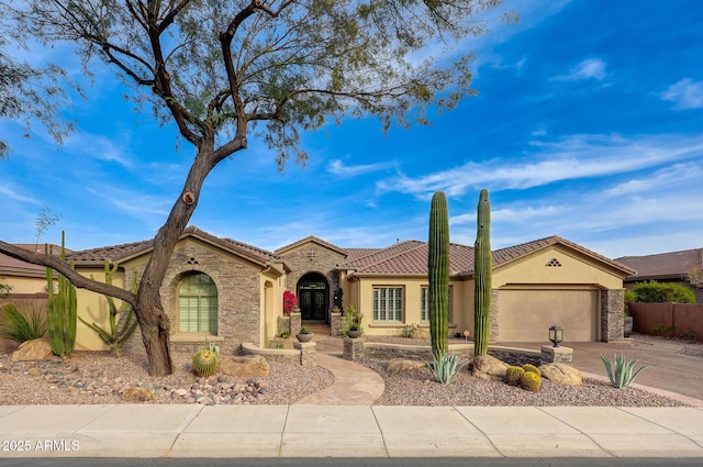 mediterranean / spanish home featuring a garage, driveway, stone siding, a tile roof, and stucco siding