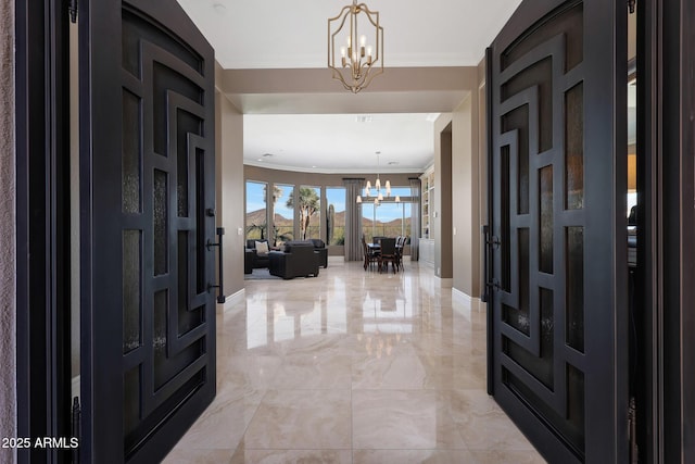 foyer with an inviting chandelier, baseboards, marble finish floor, and ornamental molding