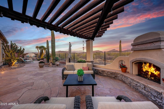 patio terrace at dusk featuring an outdoor living space with a fireplace, fence, and a pergola