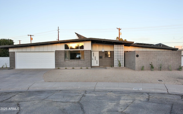 mid-century modern home featuring concrete driveway, brick siding, and an attached garage