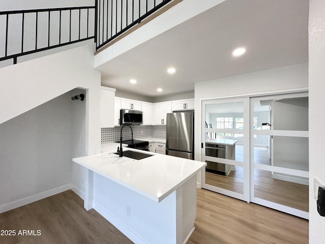 kitchen with decorative backsplash, a sink, white cabinets, light wood finished floors, and stainless steel appliances