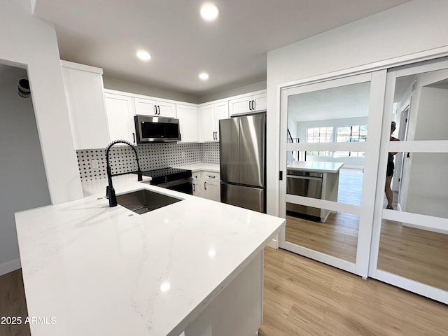 kitchen featuring decorative backsplash, light wood-style floors, white cabinets, light stone counters, and appliances with stainless steel finishes