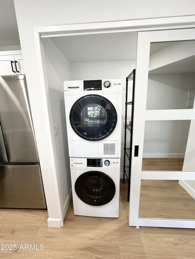 laundry area featuring baseboards, stacked washing maching and dryer, wood finished floors, and laundry area