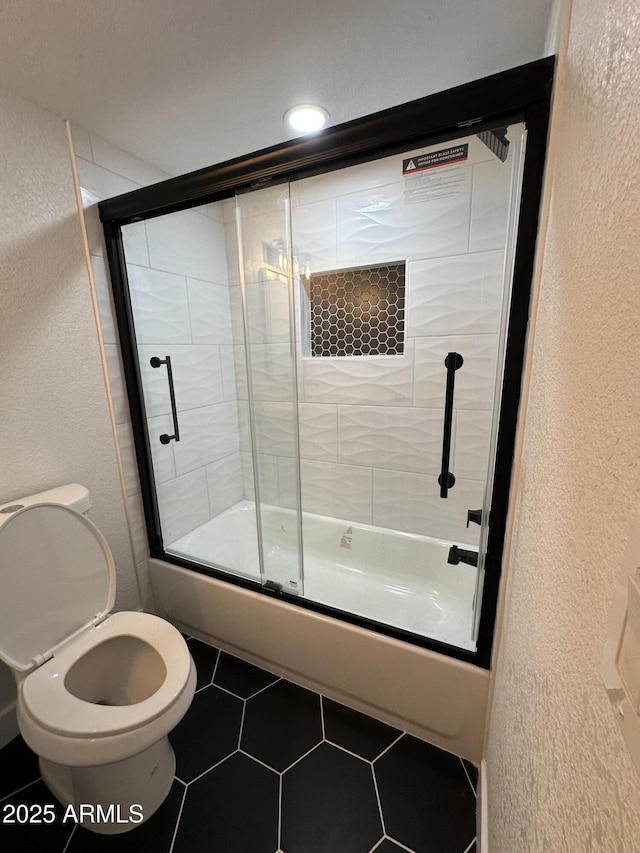 bathroom featuring bath / shower combo with glass door, a textured wall, and tile patterned flooring