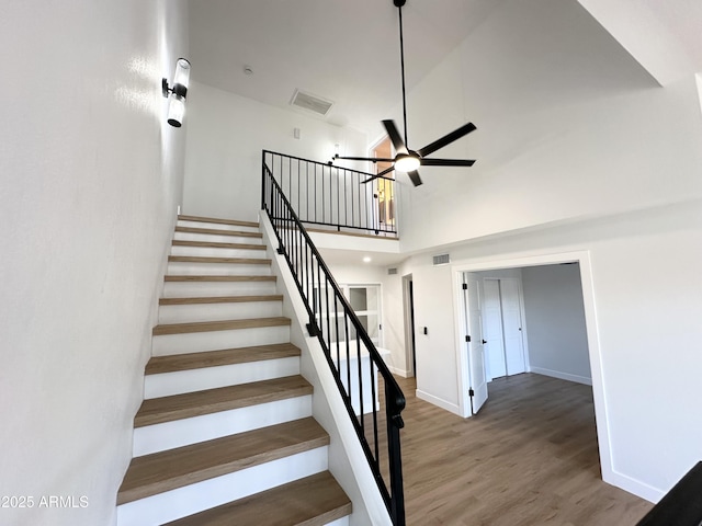stairway featuring a ceiling fan, visible vents, wood finished floors, and a towering ceiling