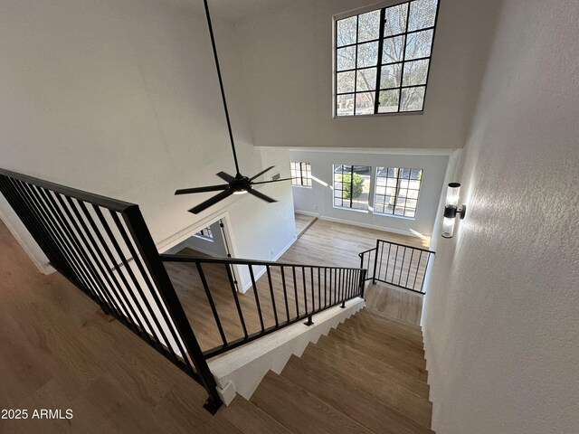 staircase featuring baseboards, a high ceiling, ceiling fan, and wood finished floors