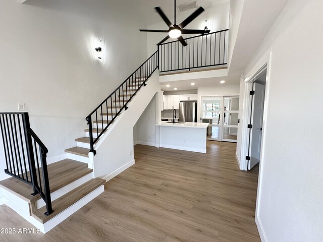 stairs with a ceiling fan, baseboards, wood finished floors, and a towering ceiling