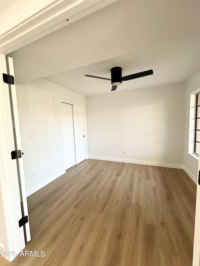 interior space with light wood-type flooring, a ceiling fan, baseboards, and a closet