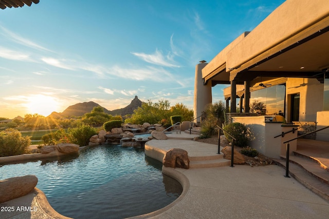 outdoor pool with a ceiling fan, a bar, a mountain view, a patio, and exterior kitchen