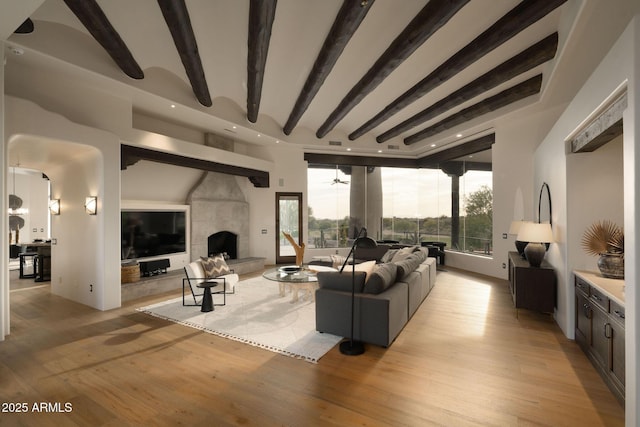 living area featuring a wealth of natural light, light wood-style flooring, beam ceiling, and a fireplace