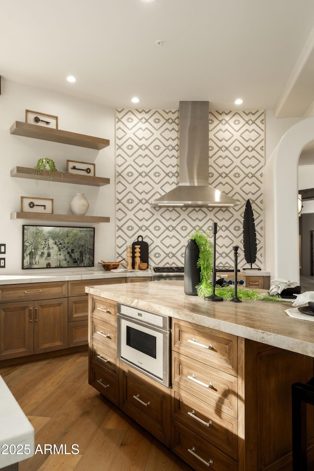 kitchen featuring open shelves, wood finished floors, decorative backsplash, light countertops, and range hood