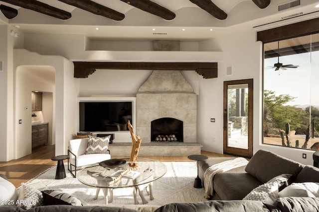 living area featuring a tile fireplace, visible vents, light wood-type flooring, beam ceiling, and ceiling fan