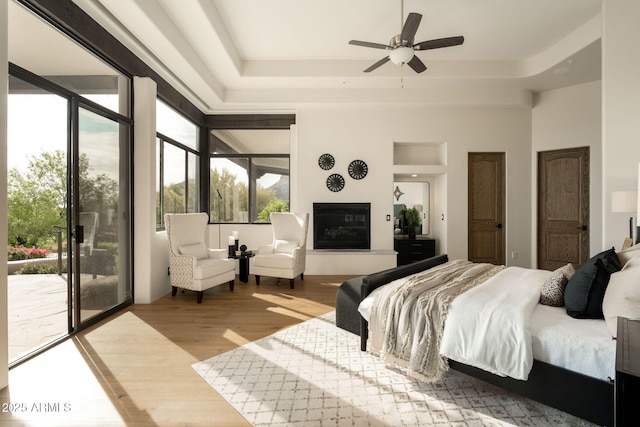 bedroom featuring multiple windows, access to outside, wood finished floors, and a raised ceiling