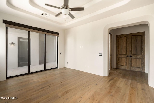 unfurnished room featuring a raised ceiling, light wood-style flooring, visible vents, and a ceiling fan