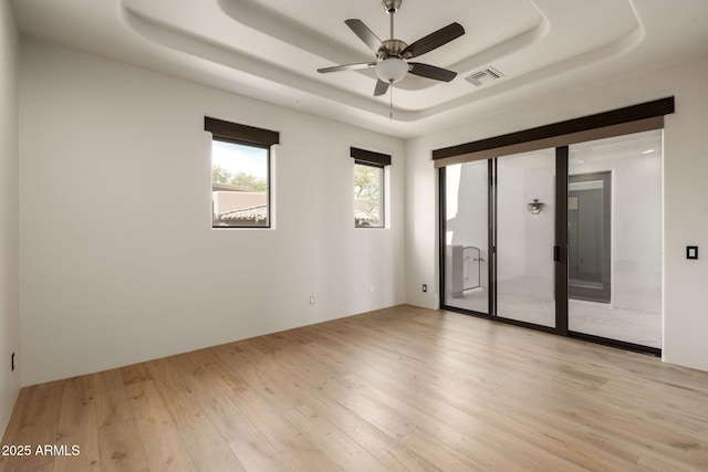 spare room featuring a ceiling fan, a tray ceiling, visible vents, and light wood-style floors