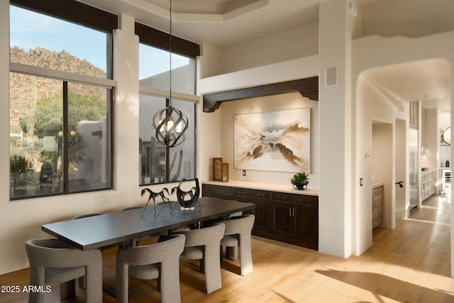 dining area featuring a towering ceiling, a chandelier, visible vents, and light wood-type flooring