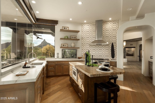 kitchen featuring recessed lighting, open shelves, a sink, wall chimney exhaust hood, and decorative backsplash
