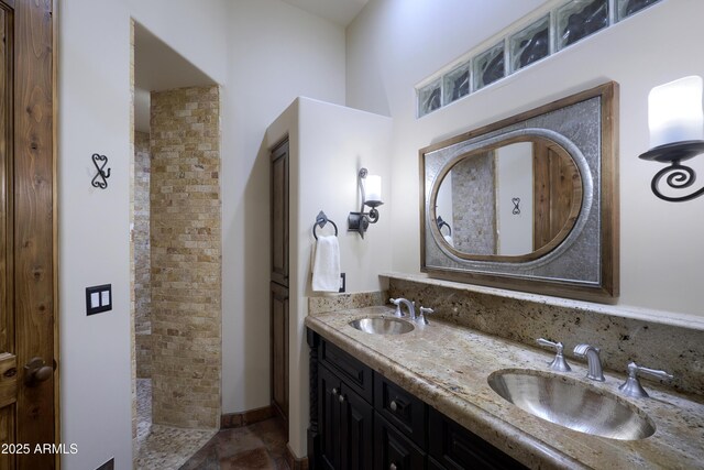 bathroom with stone finish floor, a sink, double vanity, and tiled shower