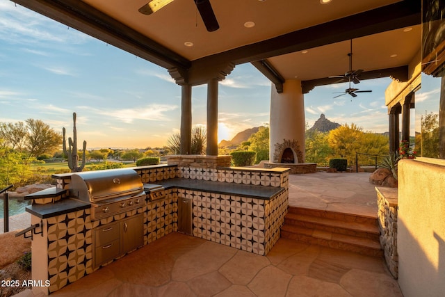 view of patio with exterior kitchen, grilling area, a ceiling fan, and a mountain view