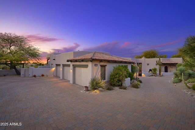 pueblo-style home with fence, a tiled roof, curved driveway, stucco siding, and a garage