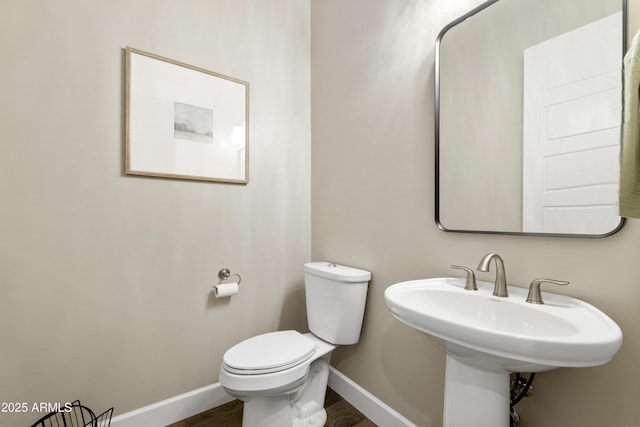 half bathroom featuring a sink, wood finished floors, toilet, and baseboards