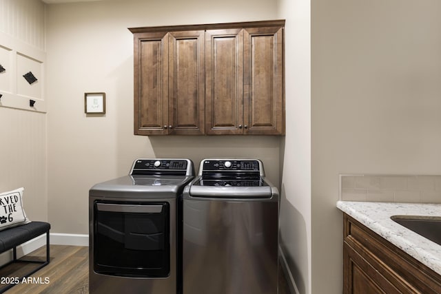 clothes washing area featuring dark wood-type flooring, cabinet space, washer and clothes dryer, and baseboards