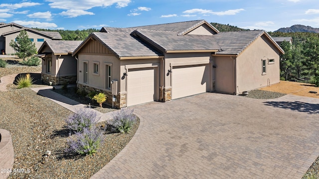 view of front facade with a garage, stone siding, decorative driveway, and stucco siding