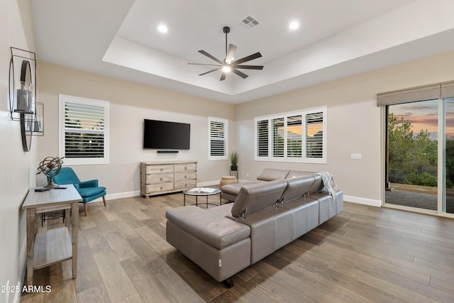 living area featuring a tray ceiling, visible vents, baseboards, and wood finished floors