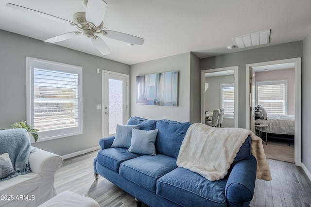 living room featuring ceiling fan, light wood-type flooring, visible vents, and baseboards