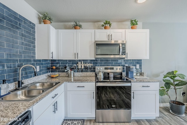 kitchen with appliances with stainless steel finishes, backsplash, a sink, and white cabinets