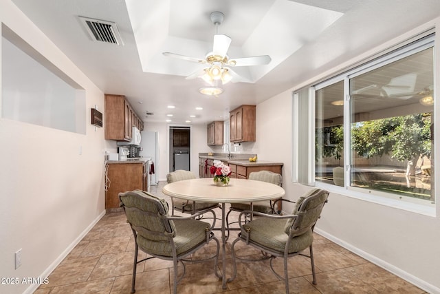 dining area featuring ceiling fan, light tile patterned floors, sink, and a tray ceiling