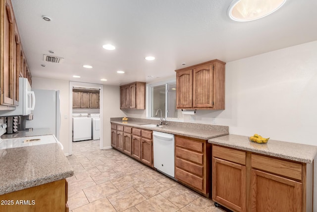 kitchen featuring washing machine and dryer, dishwasher, light stone counters, and sink