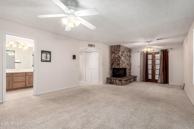 unfurnished living room featuring light carpet, ceiling fan, a stone fireplace, and a textured ceiling