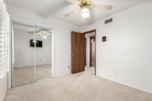 unfurnished bedroom featuring ceiling fan, light colored carpet, a closet, and a textured ceiling