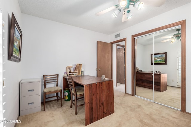 carpeted home office with ceiling fan and a textured ceiling