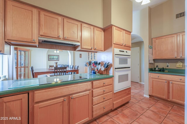 kitchen with arched walkways, light brown cabinetry, double oven, visible vents, and light tile patterned flooring