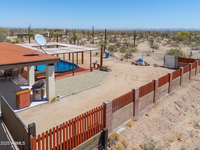 view of yard featuring view of desert, fence, a fenced in pool, and a rural view