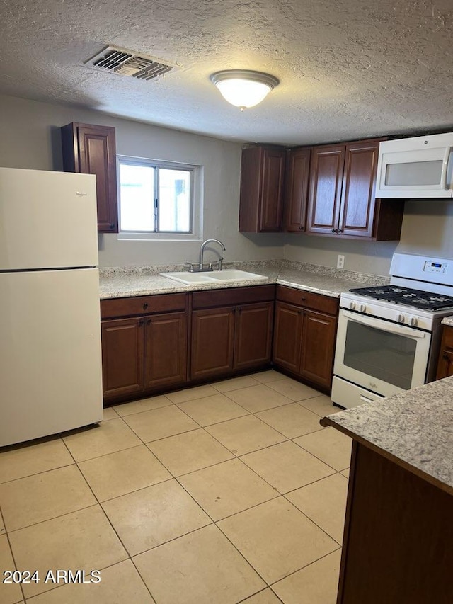 kitchen with a textured ceiling, white appliances, sink, and light tile patterned floors