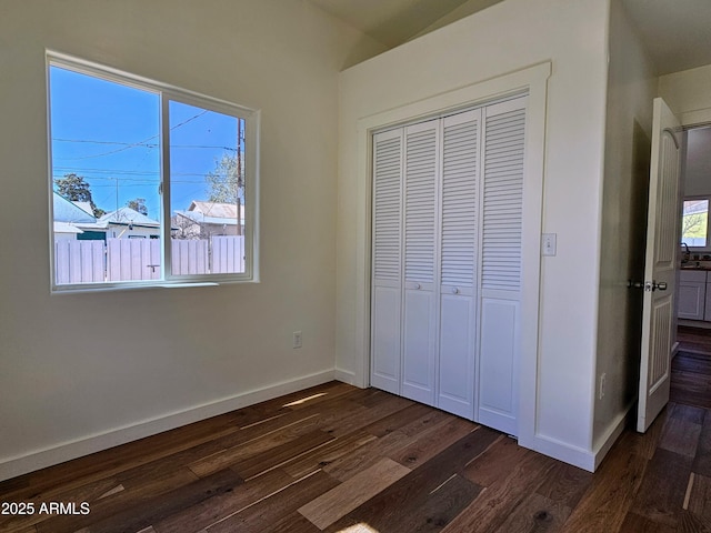 unfurnished bedroom featuring dark wood-style floors, a closet, multiple windows, and baseboards